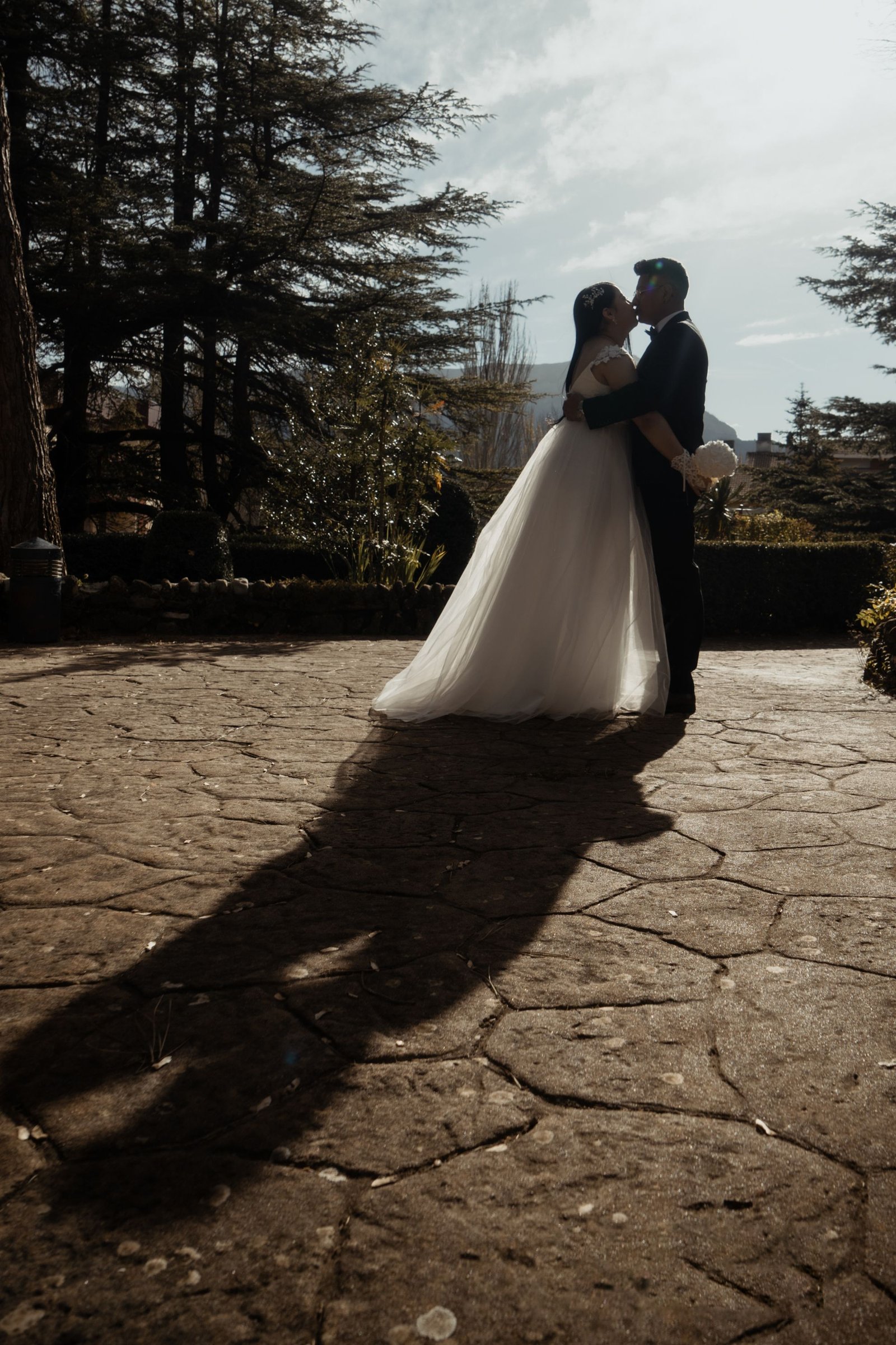 Pareja de recién casados besándose a contraluz en un jardín