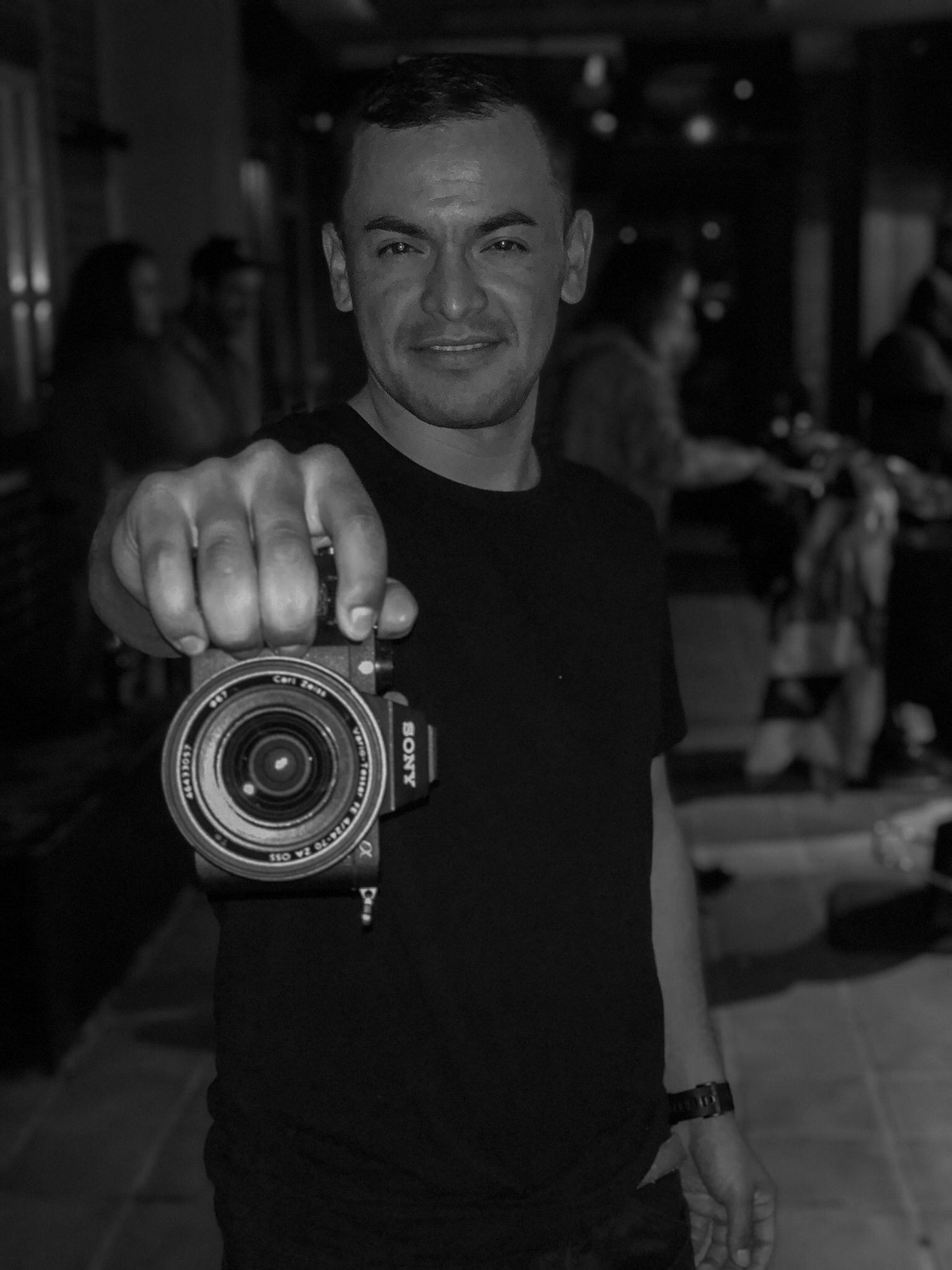 Retrato en blanco y negro de Charlie Alvarado sosteniendo una cámara